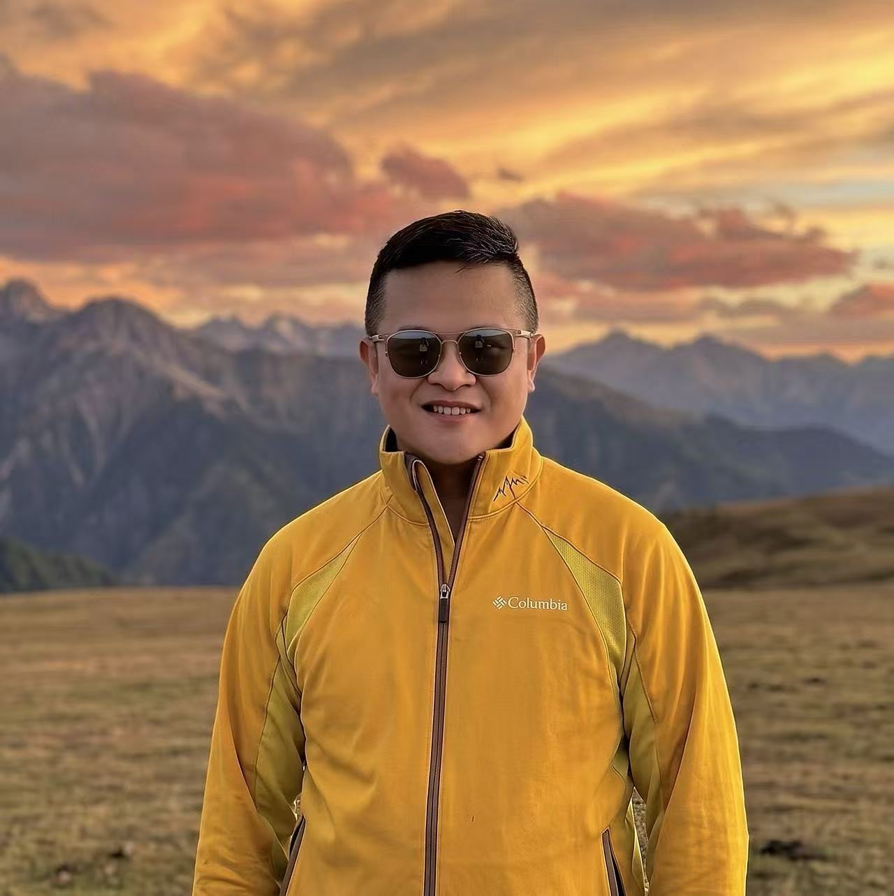 Alex standing before a mountain range beneath a golden sunset